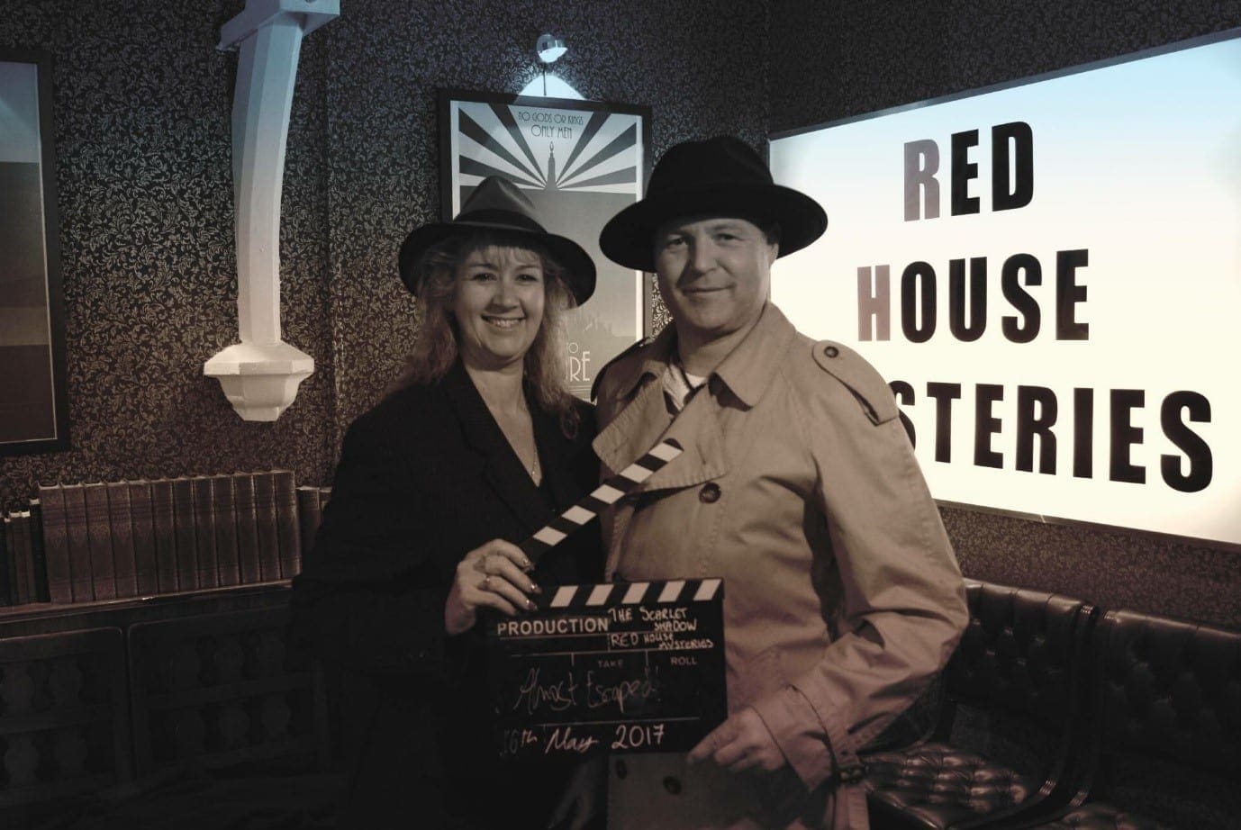 A photo of Julia and Darren with a clapperboard and in spy outfits